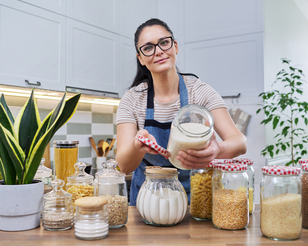 Una mujer en la cocina muestra tarros para almacenar alimentos secos.