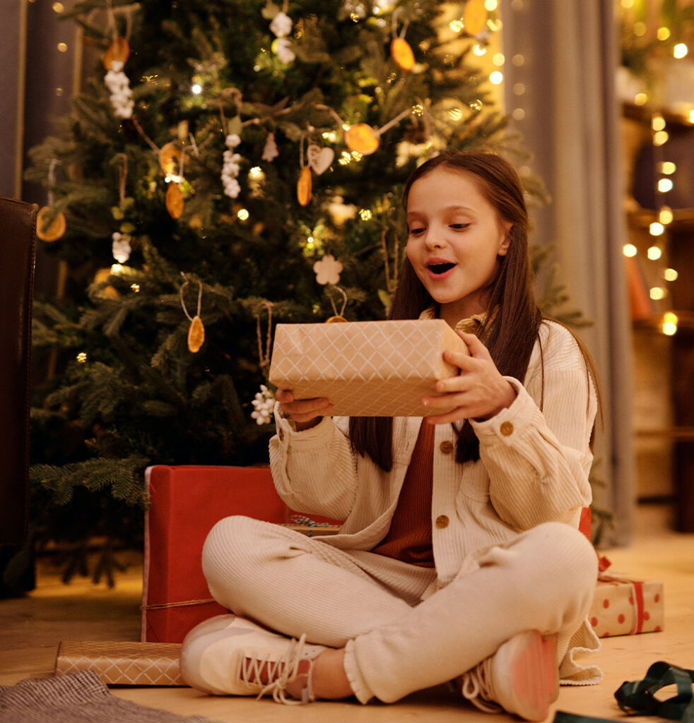 Una niña disfruta de un regalo bajo el árbol de Navidad.