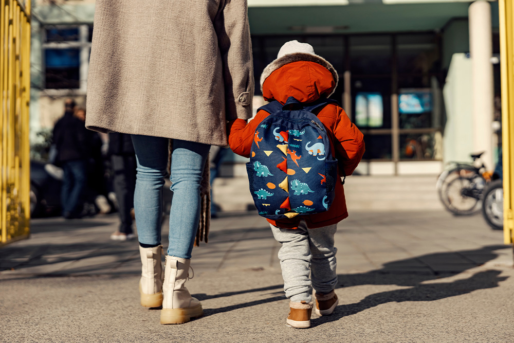 Una madre lleva de la mano a un niño en edad preescolar con una mochila