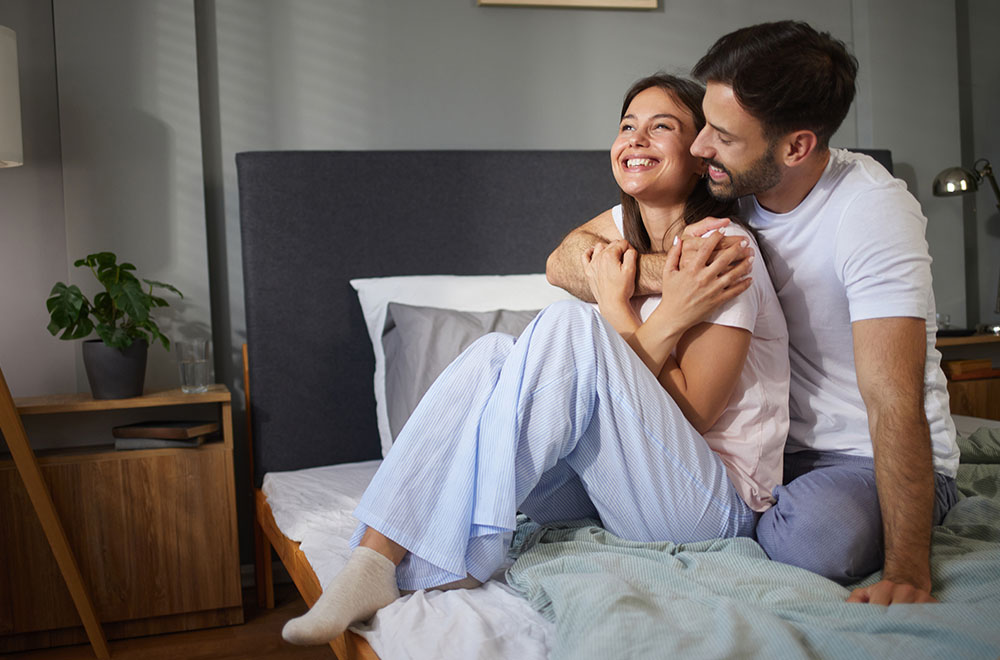 Una pareja riendo y abrazándose en la cama, compartiendo un momento acogedor y feliz juntos.