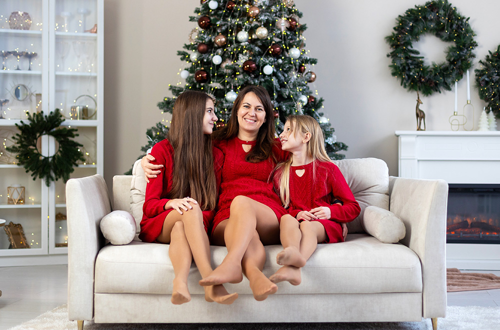 Madre y sus hijas, vestidas con vestidos rojos, pasan juntas el tiempo navideño junto al árbol.
