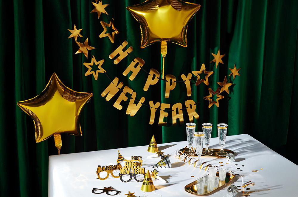 Mesa decorada para Nochevieja con globos, copas y adornos dorados.
