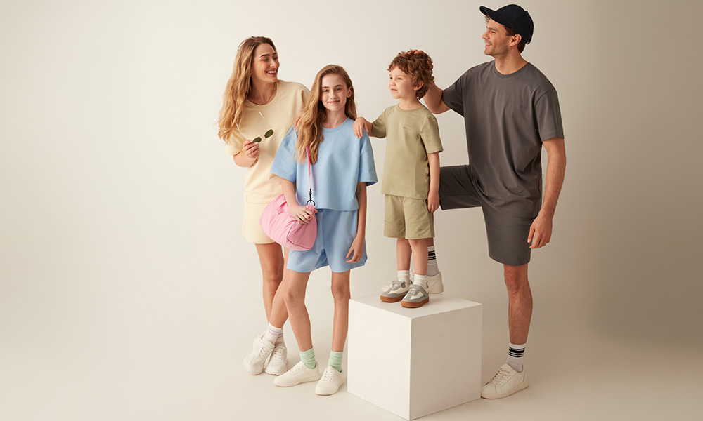 Una familia con ropa en tonos pastel posa junta sobre un fondo claro.